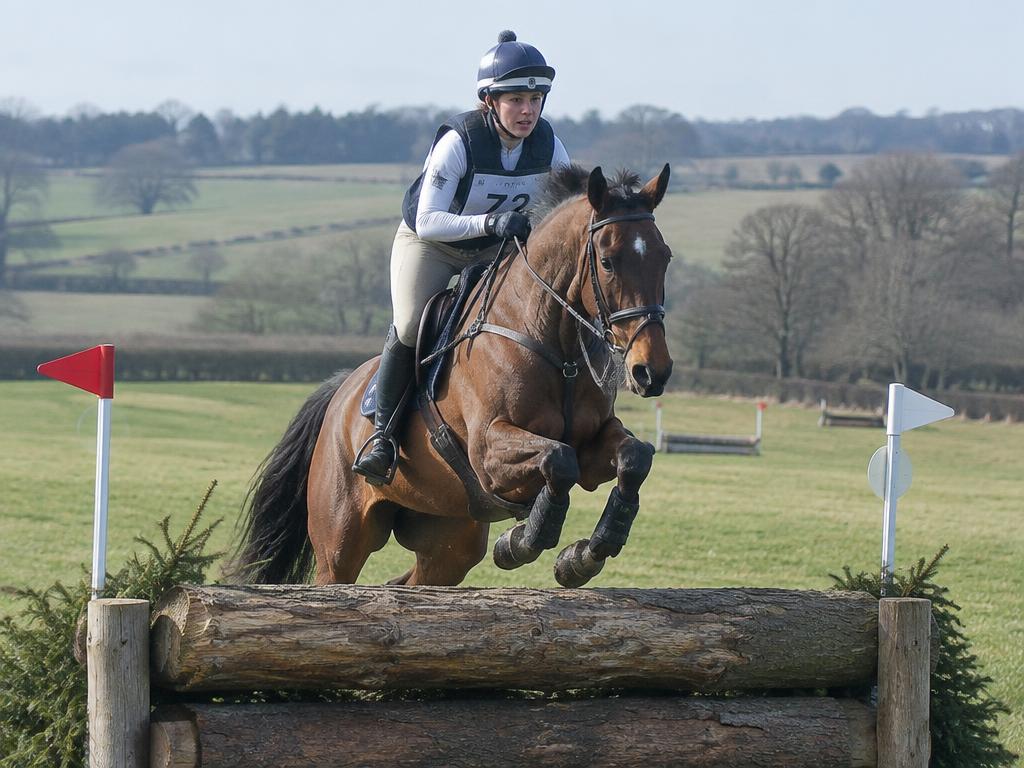 Eventer jumping a rustic log fence on a cross-country course
